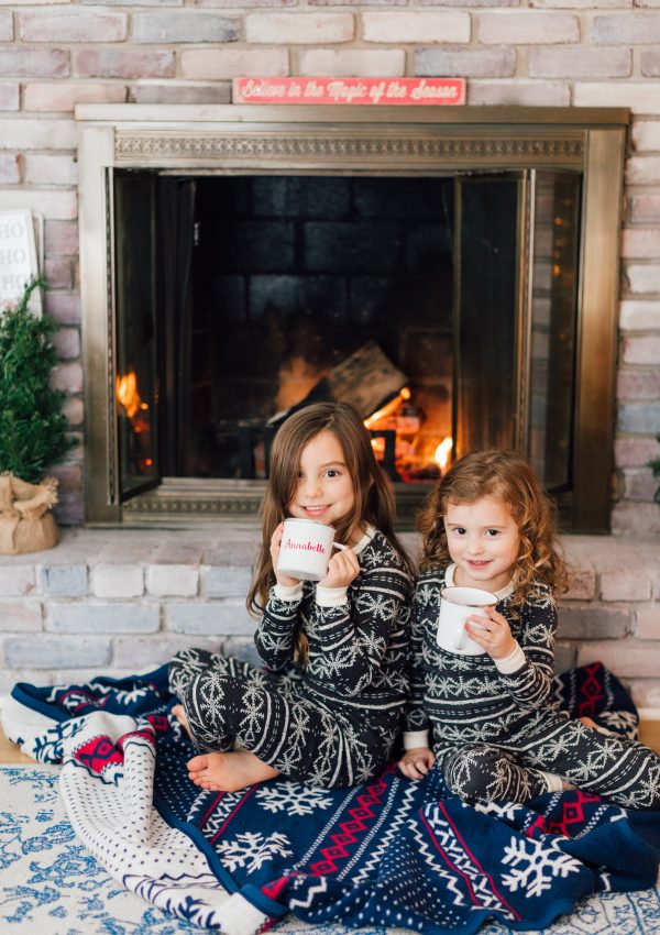 little girls drinking hot cocoa in front of fire at christmas