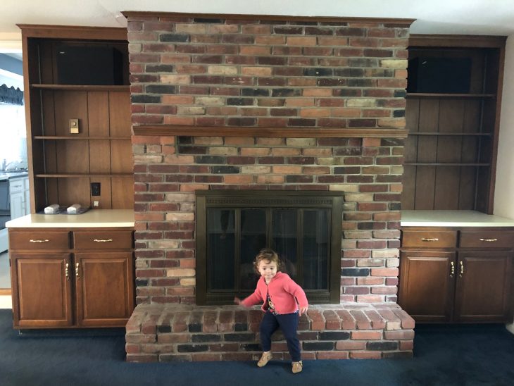 little girl sitting on brick fireplace with wood built-ins