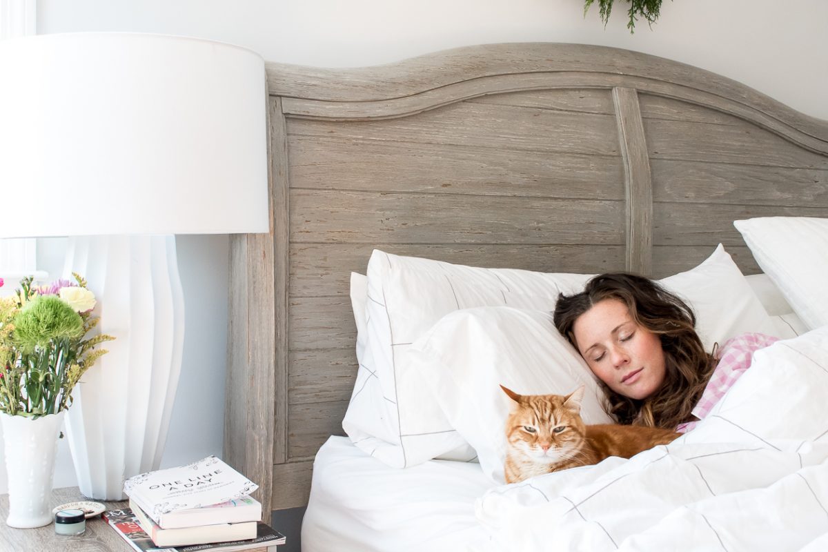 Woman in pink gingham pajamas sleeping next to an orange cat in a big bed
