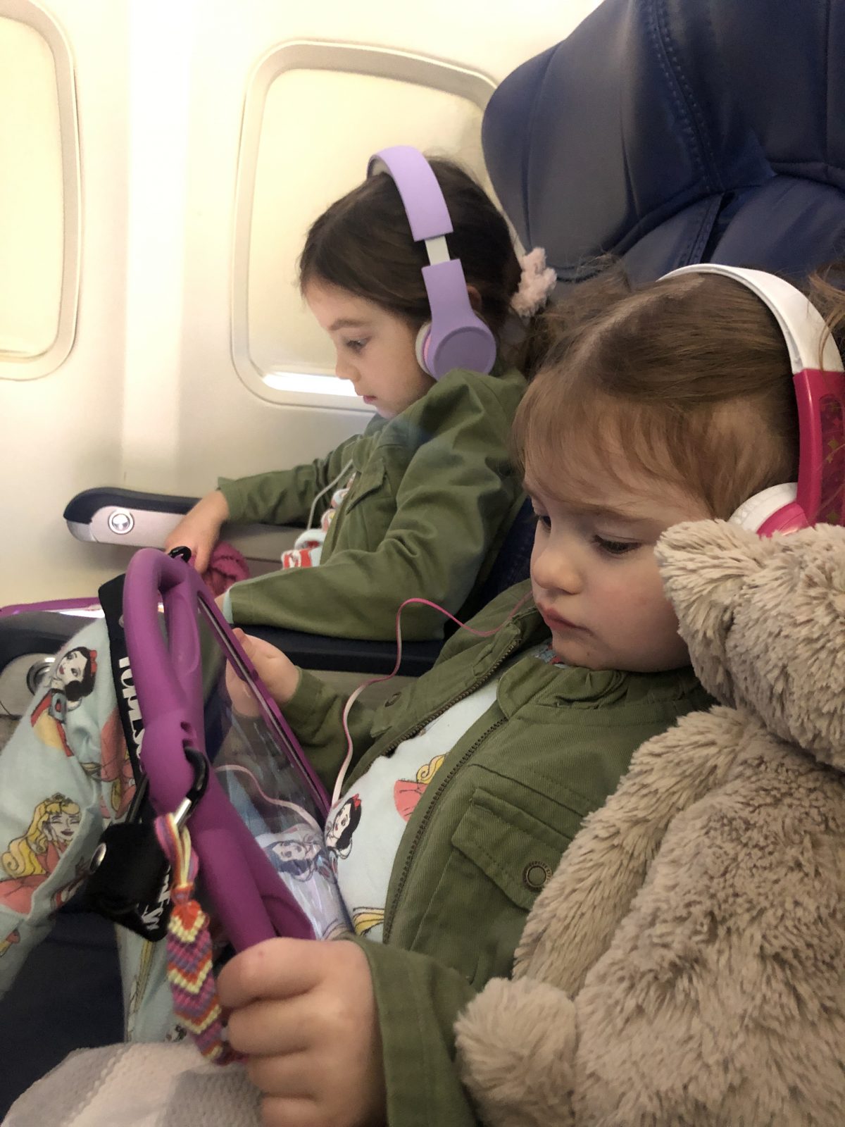 Toddlers wearing headphones and watching ipads on a plane