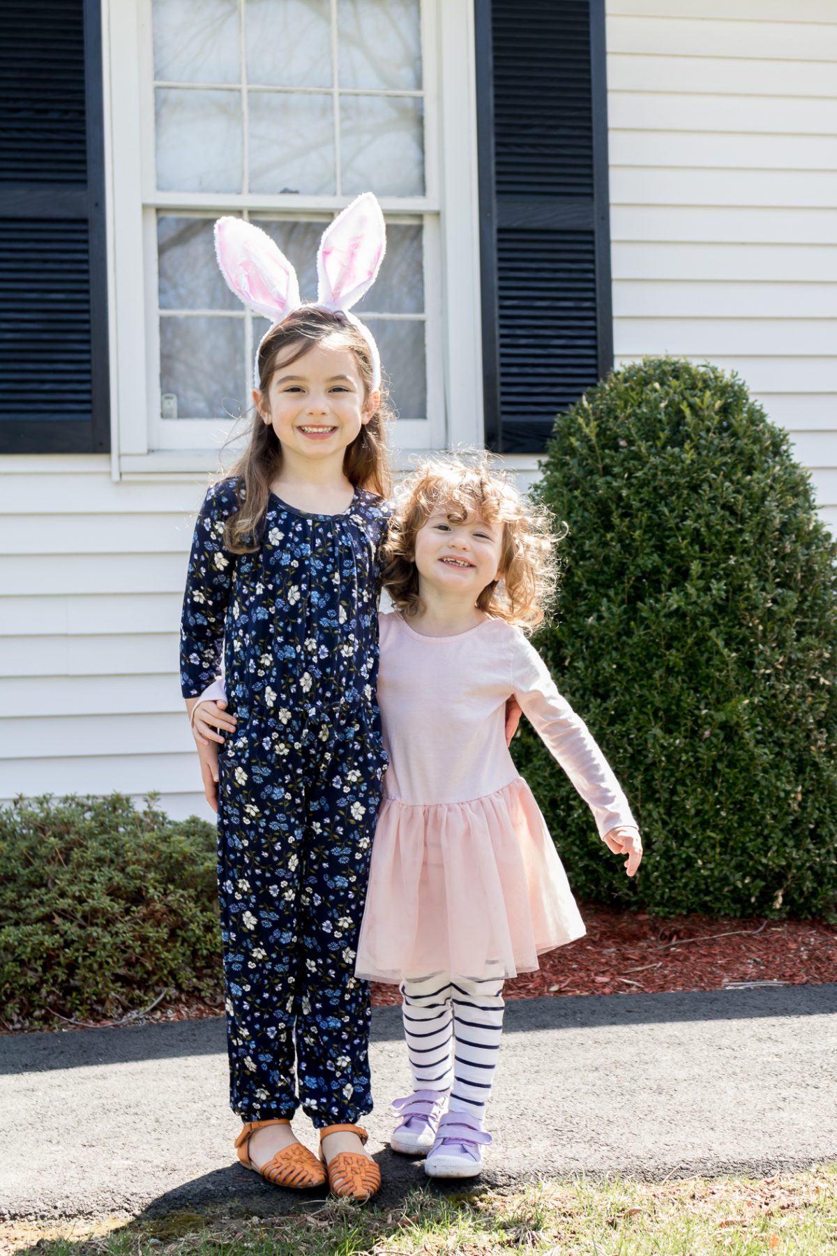 Childern - Little girl in blue jumpsuit and bunny ears and little girl with curly hair wearing a pink dress and blue striped pants
