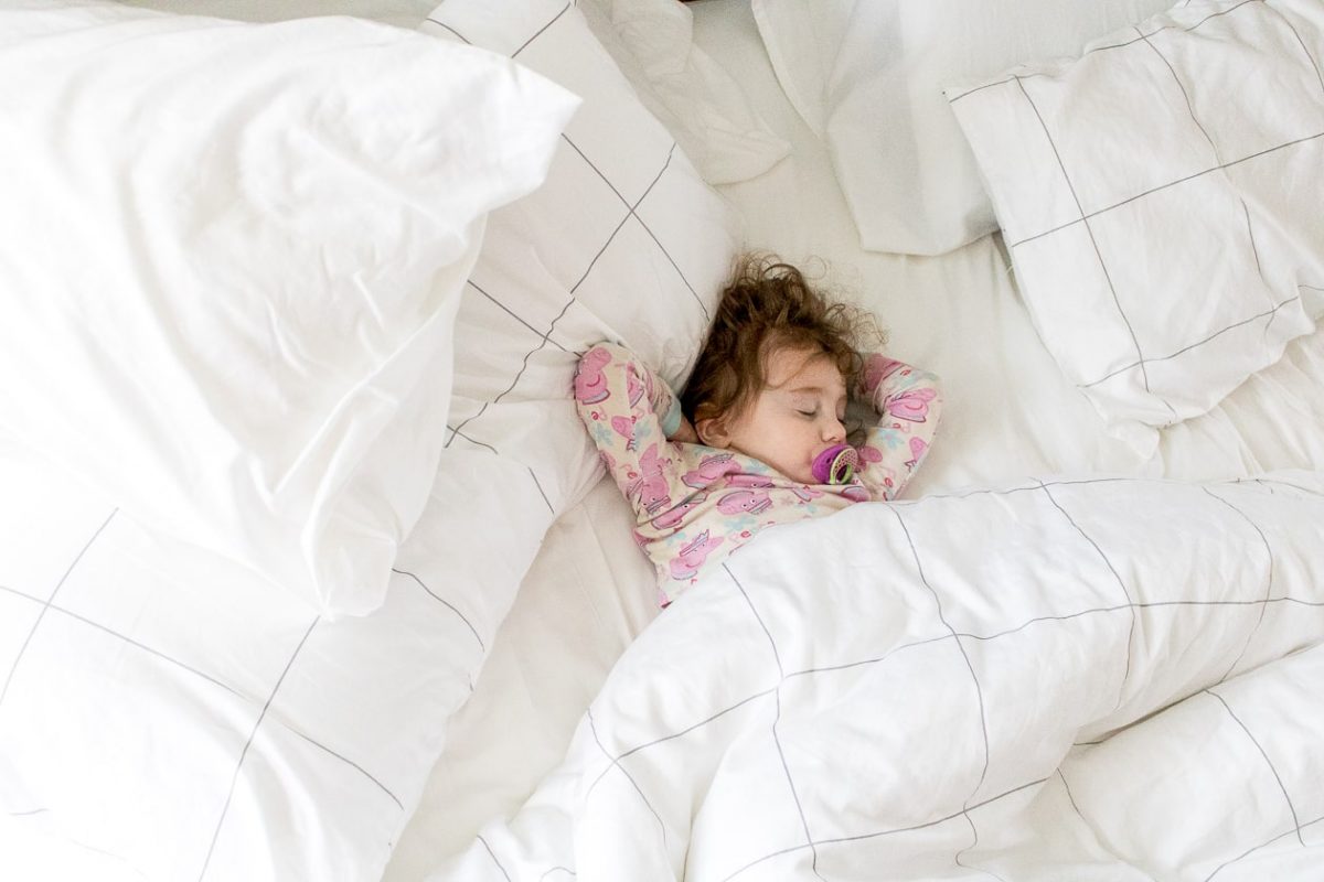 Little girl sleeping peacefully in bed with arms above her head