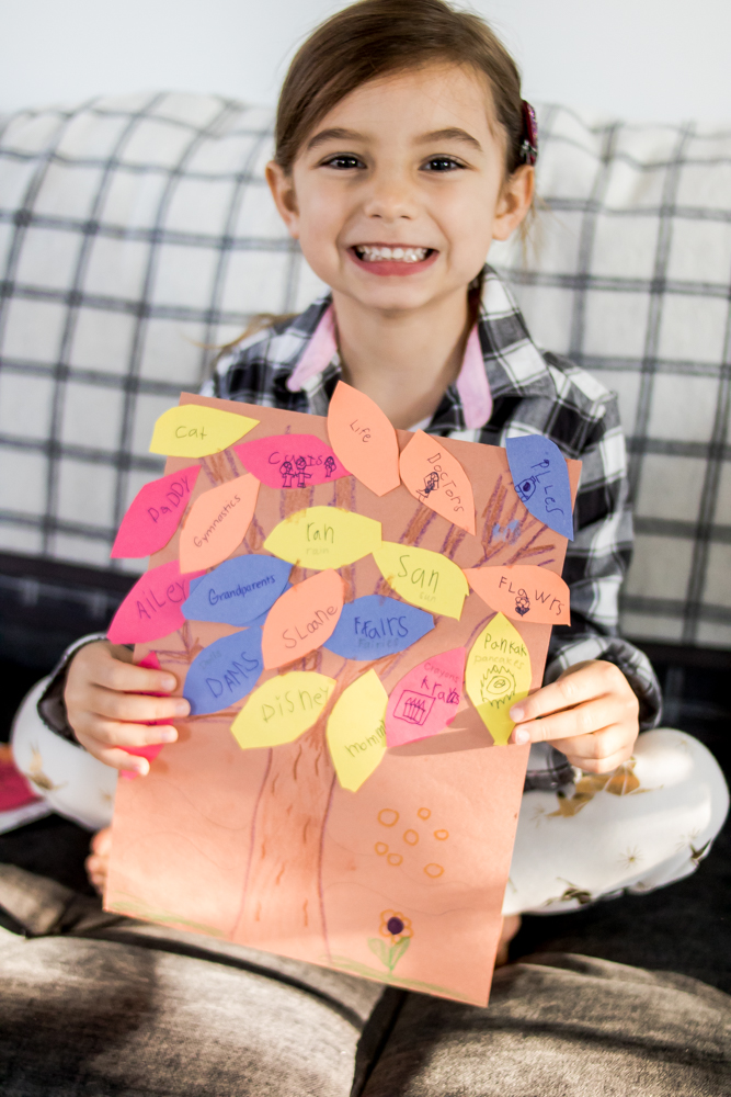 Little girl wearing plaid holding a gratitude tree