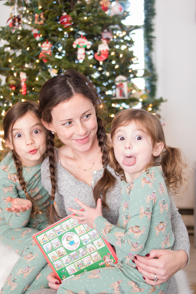 Mom looking at daughters making silly faces wearing pajamas in front of Christmas tree after stomach flu subsides