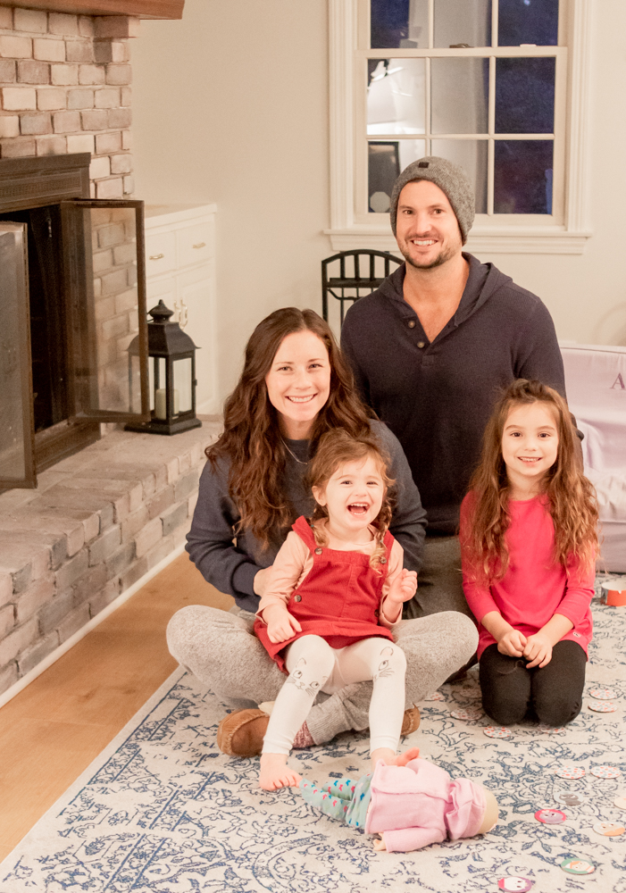 family sitting on rug smiling in front of fireplace