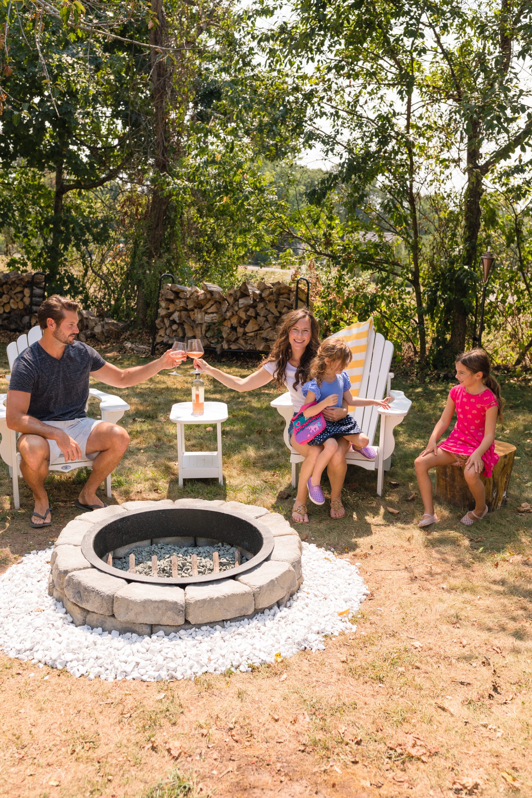 Family sitting in Adirondack chairs around stone fire pit in late August 2020