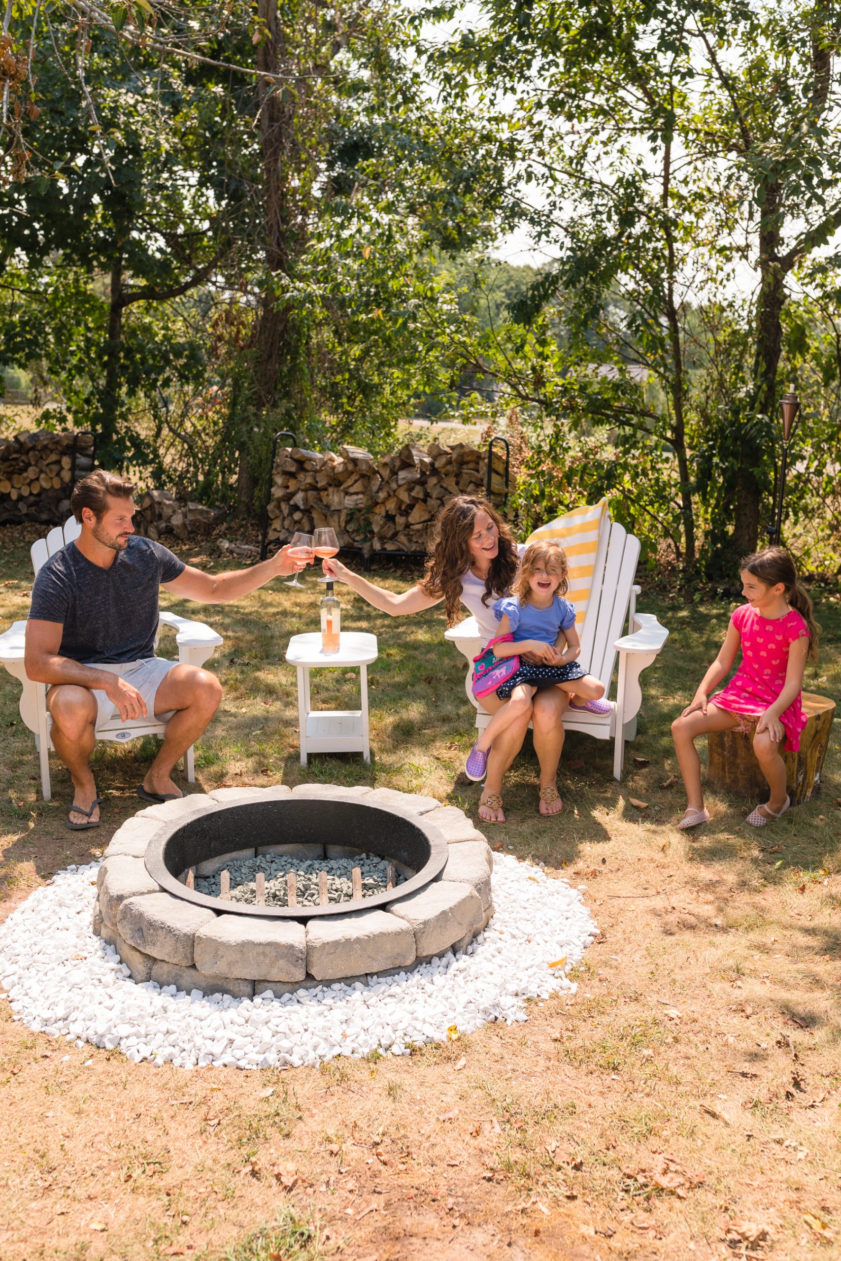 Family sitting in Adirondack chairs around stone fire pit in late August 2020