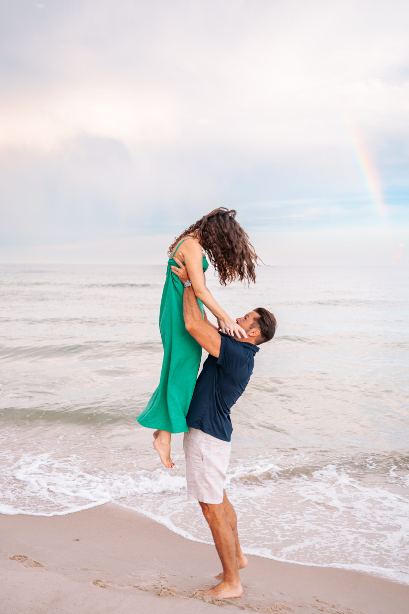 man lifting woman in air couples photo at beach navy and green outfits rainbow